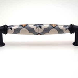 May include: A black ceramic cabinet pull with a white and grey patterned design. The pattern features geometric shapes and a subtle orange accent.