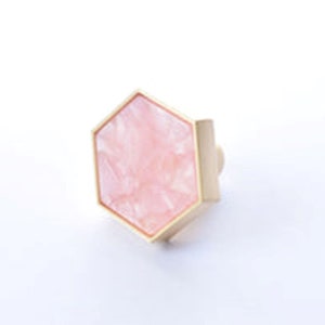 May include: A hexagonal pink and gold cabinet knob with a geometric design.