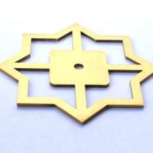 May include: A gold-coloured, star-shaped decorative element with an eight-pointed design. The centre features a square with a small hole. The edges are sharp and angular, creating a geometric pattern. The item is likely made of metal.