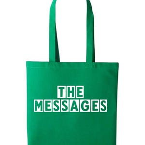 May include: A green tote bag featuring the white text "THE MESSAGES". The bag has a rectangular design and a matching green handle, suitable for carrying items.