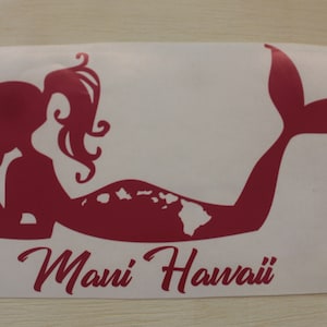 Puede incluir: Una pegatina de vinilo roja de una sirena con un contorno de las islas hawaianas en su cola. El texto "Maui Hawaii" está escrito debajo de la sirena.