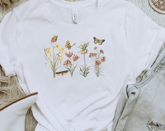 May include: White t-shirt with a floral print featuring butterflies and flowers in shades of pink, yellow, and green.