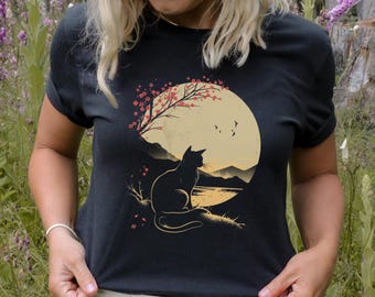Op de afbeelding: Zwart T-shirt met een afbeelding van een zwarte kat die voor een volle maan zit met een kersenbloesemboom en een meer op de achtergrond.