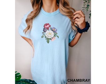 Puede incluir: Una camiseta azul claro con un estampado floral de flores rosas, blancas y moradas. Las flores están dispuestas en un ramo y tienen hojas verdes.