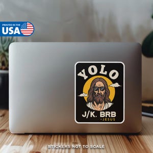 May include: A rectangular sticker with the text "YOLO J/K. BRB - JESUS" and an illustration of Jesus wearing sunglasses. The sticker is on a laptop. The words "PRINTED IN THE USA" are also visible.