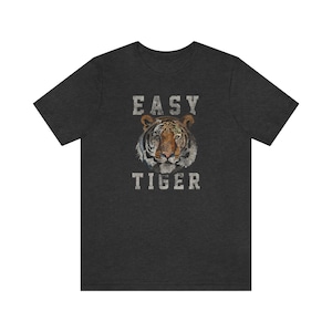 K&ouml;nnte beinhalten: Ein dunkel-melierter grauer T-Shirt mit einem abgenutzten wei&szlig;en Grafikdruck eines Tigergesichts und dem Text "EASY TIGER".