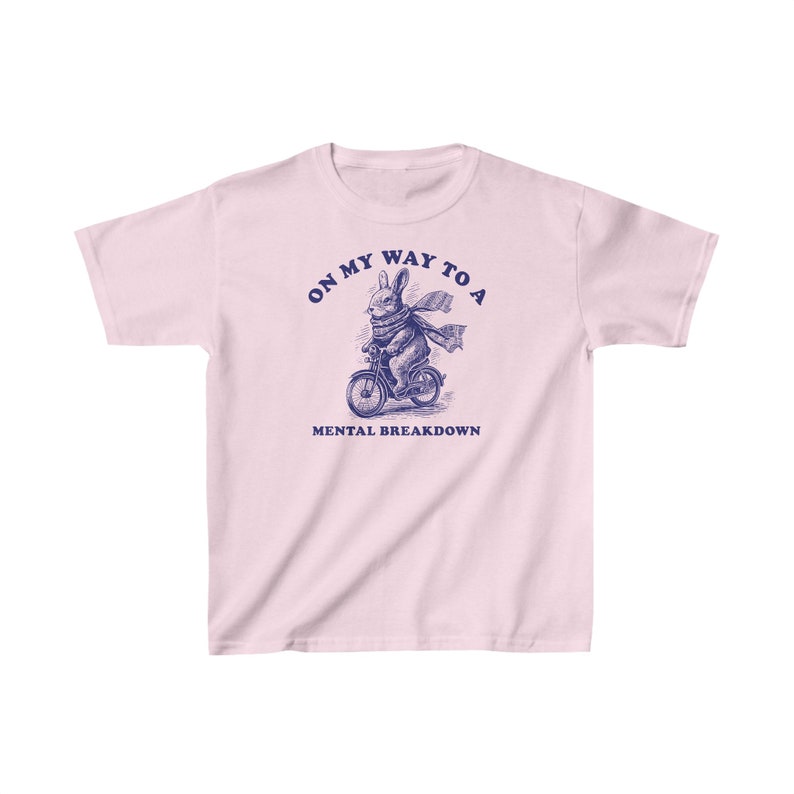May include: Pink t-shirt featuring a blue illustration of a rabbit riding a bicycle. The text "On my way to a mental breakdown" is printed on the shirt.