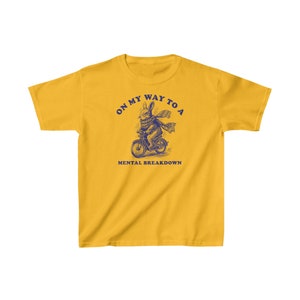 May include: Yellow t-shirt with a blue illustration of a rabbit riding a bicycle. The text "On my way to a mental breakdown" is printed on the shirt.