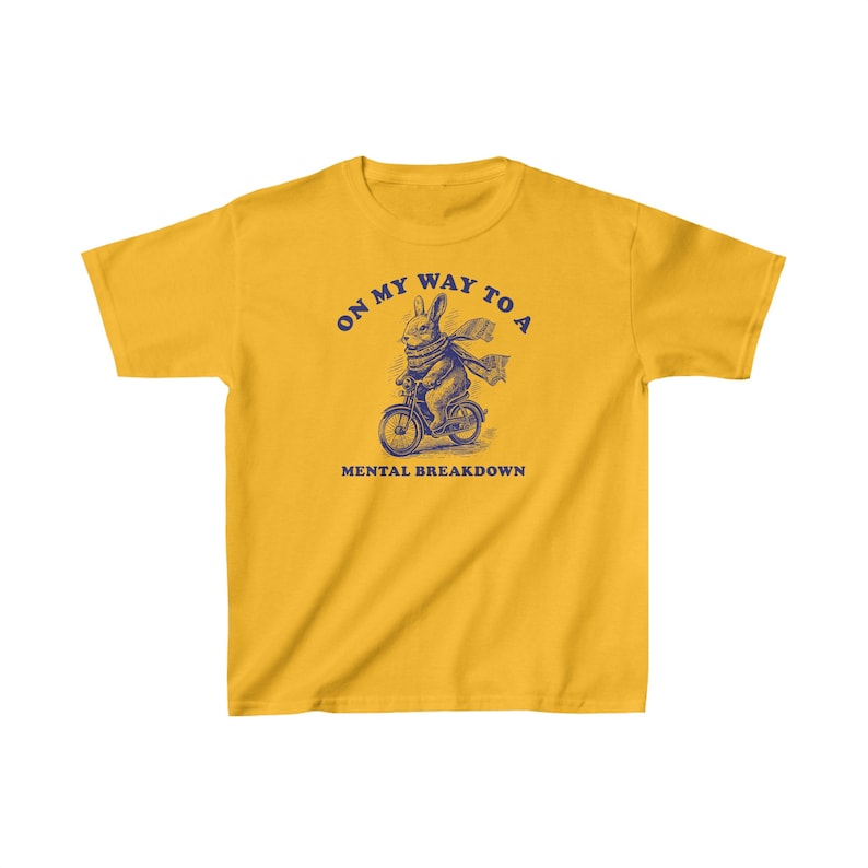 May include: Yellow t-shirt with a blue illustration of a rabbit riding a bicycle. The text "On my way to a mental breakdown" is printed on the shirt.