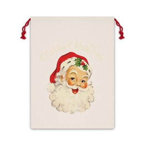 May include: A cream-colored drawstring bag featuring a vintage illustration of Santa Claus in a red hat with holly accents. The words "Merry Christmas" are written in gold script above Santa's head. The bag has red drawstrings.