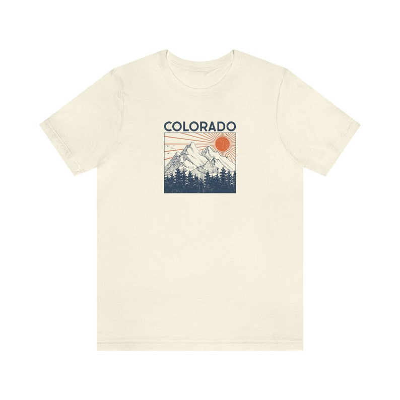 May include: A cream colored t-shirt with a vintage style graphic of a mountain range with a red sun and the word "COLORADO" printed in blue.