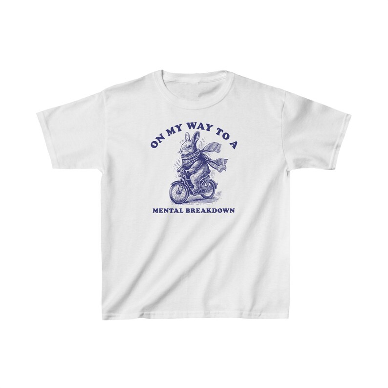 May include: White t-shirt featuring a blue illustration of a rabbit riding a bicycle. The text "On my way to a mental breakdown" is printed below the image.
