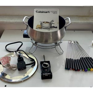 May include: A Cuisinart fondue set with a stainless steel pot, stand, and forks. The set includes a control unit, a power cord, and a recipe booklet. The forks have colored tips. The pot has two handles.