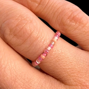 Op de afbeelding: Een roze en witte kralenring met iriserende kralen.