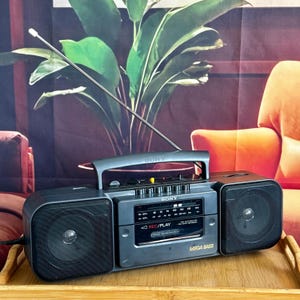 May include: A dark grey Sony portable radio cassette player featuring a long silver telescopic antenna, dual speakers, a top handle, and a central control panel with the text SONY, REC/PLAY, and MEGA BASS printed on the front casing.