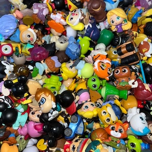 May include: A collection of colorful, small character figurines, including Mickey Mouse, Rapunzel, and other cartoon characters. The figurines are made of plastic and feature various colors and designs. The image shows a variety of characters, with some figurines partially visible.