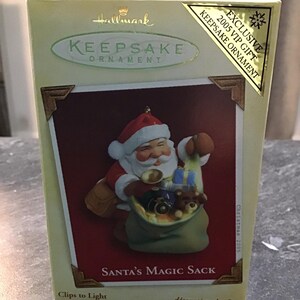 Könnte beinhalten: Ein Hallmark Keepsake Ornament, das den Weihnachtsmann mit einem großen Sack voller Spielzeug zeigt. Das Ornament trägt den Titel "Santa's Magic Sack" und ist Teil der VIP-Geschenk-Kollektion 2005.
