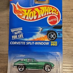 May include: A green Corvette Split-Window die-cast toy car in its original packaging. The packaging is blue with the Hot Wheels logo and the text "NEW!" and "COLLECTOR #447". The car is metallic green.