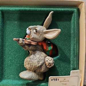 May include: A 1981 Hallmark Christmas ornament featuring a brown rabbit playing a fiddle. The ornament is in its original box and is labeled "The Friendly Fiddler".