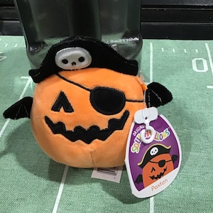 May include: Orange and black plush pumpkin with a pirate hat and eye patch. The plush toy is labelled "Paxton" and is part of the "Original Squishmallows" collection.