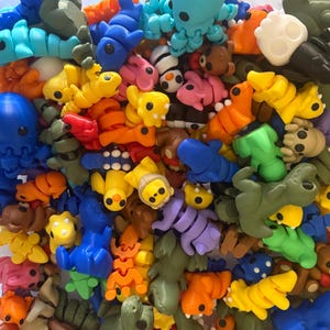 May include: A collection of colorful, small, plastic figurines in various shapes and designs. The figurines are mostly animal-themed, with some abstract shapes and a few human-like figures. The figurines are arranged in a random pattern, creating a visually appealing and playful scene.