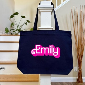 K&ouml;nnte beinhalten: Eine marineblaue Tragetasche mit einem pinkfarbenen "Emily"-Design in einer Retro-Schrift.