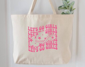 May include: A beige tote bag with pink text that reads "Let's Go Girls" and a pink cowboy hat with stars. The bag has a pink and white design.