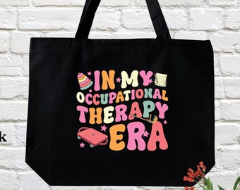 May include: Black canvas tote bag with the text "In My Occupational Therapy Era" in colorful retro font. The text is surrounded by small illustrations of occupational therapy tools.