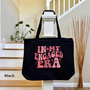 May include: Black tote bag with the text "In My Engaged Era" in pink and white lettering with a ring and stars.