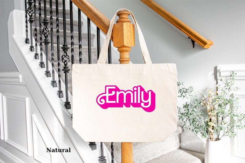 K&ouml;nnte beinhalten: Eine nat&uuml;rliche Canvas-Tragetasche mit dem Namen "Emily" in pinken Buchstaben.