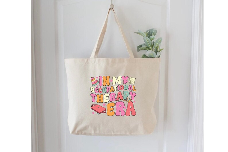 May include: A beige canvas tote bag with the text "In My Occupational Therapy Era" in colorful letters and illustrations.