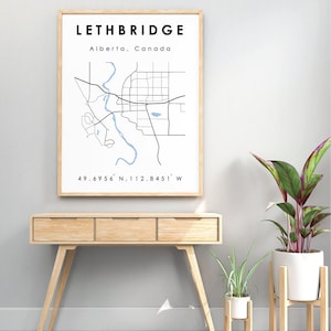 Puede incluir: Una impresión de mapa en blanco y negro de Lethbridge, Alberta, Canadá. El mapa muestra las calles de la ciudad y el río Oldman. El texto "Lethbridge, Alberta, Canadá" y "49.6956° N, 112.8451° W" está impreso debajo del mapa.