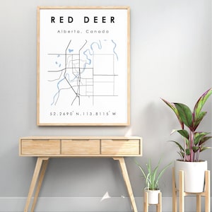 May include: A framed print of a map of Red Deer, Alberta, Canada. The map shows the city's streets and waterways. The text "Red Deer, Alberta, Canada" and "52.2690° N, 113.8115° W" are printed below the map.