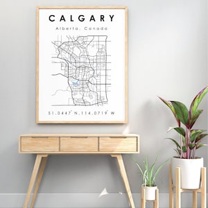 May include: A framed print of Calgary, Alberta, Canada, featuring a detailed black and white map of the city. The print includes the city's name, province, and coordinates. The artwork is displayed above a wooden console table.