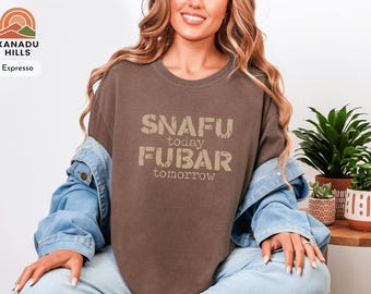 May include: Espresso-coloured t-shirt with the text "SNAFU today FUBAR tomorrow" in a distressed font. The shirt is part of the Xanadu Hills collection. The model is wearing a denim jacket.