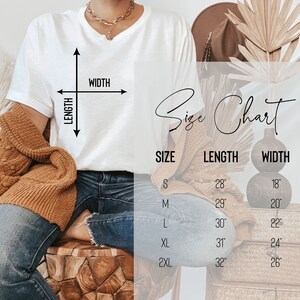 Pode incluir: Uma camiseta branca com uma tabela de tamanhos sobreposta. A tabela exibe os tamanhos S a 2XL, com as medidas de comprimento e largura correspondentes em polegadas. A camiseta est&aacute; sendo modelada, com um colar de ouro e um su&eacute;ter marrom.