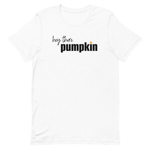 Pode incluir: Camiseta branca com a frase "hey there pumpkin" em preto, em escrita cursiva e letras de bloco, com um pequeno gr&aacute;fico de ab&oacute;bora laranja. Uma pe&ccedil;a casual.