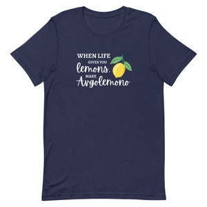 Puede incluir: Una camiseta azul marino de manga corta con un gr&aacute;fico de un lim&oacute;n amarillo con hojas verdes. El texto impreso en blanco dice: WHEN LIFE GIVES YOU lemons. MAKE Avgolemono. El dise&ntilde;o est&aacute; centrado en el pecho de la prenda de cuello redondo.