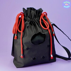 May include: Black drawstring bag with red drawstrings and a black strap. The bag has a large hole in the front and several smaller holes.