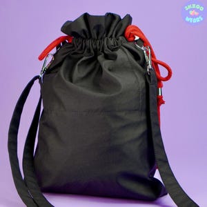 May include: Black drawstring bag with a red drawstring and a black shoulder strap. The bag has a small pocket on the front.