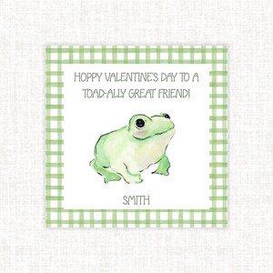 May include: A square card with a green gingham border features a watercolor illustration of a light green frog. The text reads "Hoppy Valentine's Day to a Toad-ally Great Friend!" and the name "SMITH" is printed below the frog.