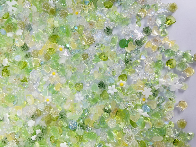 May include: A variety of green, clear, and white resin embellishments in the shape of flowers, hearts, and leaves. The embellishments are scattered on a white background.
