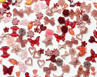 May include: A collection of assorted decorative embellishments in shades of red, pink, and glittery gold. The assortment includes bows, stars, butterflies, hearts, flowers, and candies. These small, decorative items are ideal for crafting and adding flair to various projects.