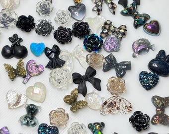 May include: A collection of various resin embellishments in different shapes and colors. The assortment includes bows, roses, hearts, butterflies, and teddy bears. Colors range from black and white to iridescent and glittery, suitable for crafts and nail art.