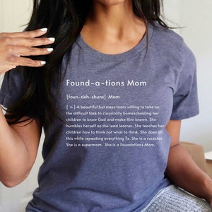 May include: A navy blue t-shirt with the text "Found-a-tions Mom [foun-deh-shuns] Mom [n.] A beautiful hot mess mom willing to take on the difficult task to classically homeschooling her children to know God and make Him known. She humbles herself as the lead learner. She teaches her children how to think not what to think. She does all this while repeating everything 7x. She is a rockstar. She is a supermom. She is a Foundations Mom."