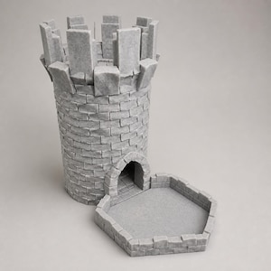 May include: A gray dice tower shaped like a cylindrical stone castle turret with a crenelated top and a stone-textured exterior. The structure features a central arched doorway leading to an attached hexagonal tray with low stone walls for dice.