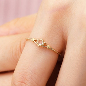 Könnte beinhalten: Ein zarter Goldring mit einem kleinen, klaren Edelstein, der in einem floralen Design gefasst ist.