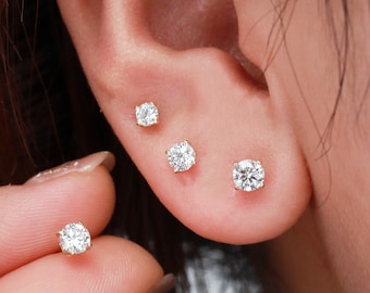 Könnte beinhalten: Nahaufnahme eines Ohrs mit drei kleinen Diamant-Ohrsteckern. Die Ohrringe sind in verschiedenen Größen und in Gold gefasst.