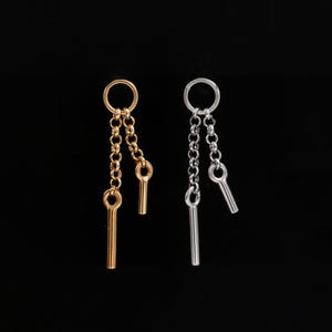 May include: A pair of drop earrings, one gold-toned and one silver-toned, each featuring a circular hoop at the top connected to two short, delicate chains of varying lengths, with each chain ending in a small, smooth, cylindrical metal bar pendant.