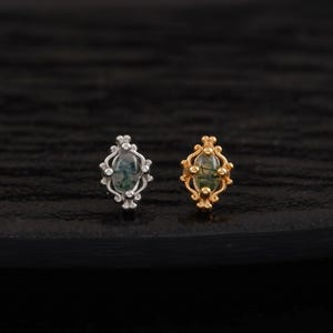Peut inclure: Deux boucles d'oreilles à clous ornées. L'une est argentée avec une pierre verte, l'autre est dorée avec une pierre verte. Les deux boucles d'oreilles ont un design ovale avec une petite pierre ronde au centre.